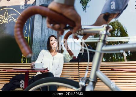 Immagine ritagliata di uomo d'affari con la bicicletta che parla con il collega a. bar sul marciapiede Foto Stock