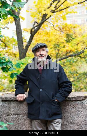 Ritratto di uomo anziano sicuro in piedi con la mano in tasca nel parco durante l'autunno Foto Stock