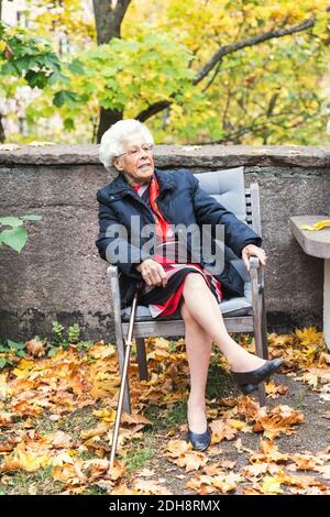 Intera lunghezza della donna anziana seduta sulla sedia nel parco Foto Stock