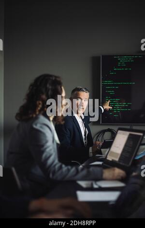 Uomo d'affari che punta allo schermo di proiezione mentre discute con il collega a. luogo di lavoro Foto Stock