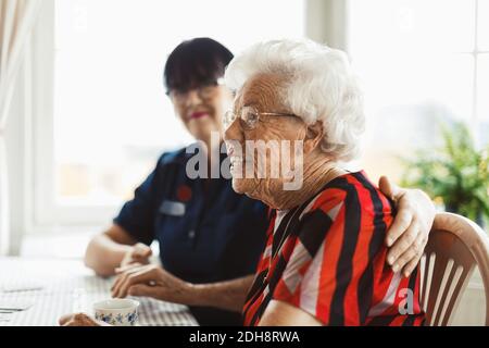 Vista laterale di donna anziana felice seduta con custode a. casa Foto Stock