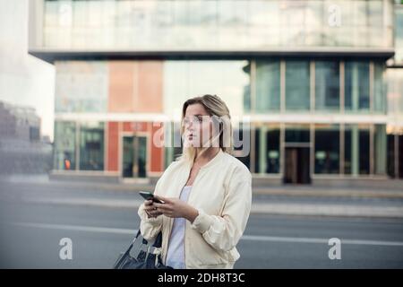 Giovane donna con telefono cellulare che cammina in città Foto Stock