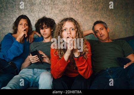 Ragazza che prega mentre guarda gli sport con la famiglia a casa Foto Stock