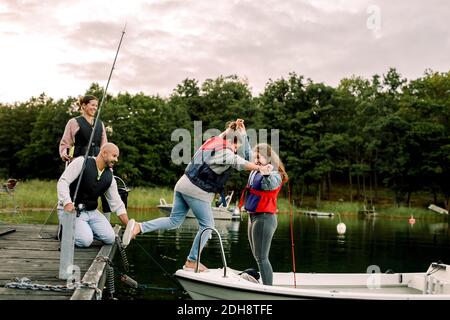 Genitori che guardano sorridendo figlia che tiene la mano della sorella mentre si è in piedi in barca sul lago Foto Stock