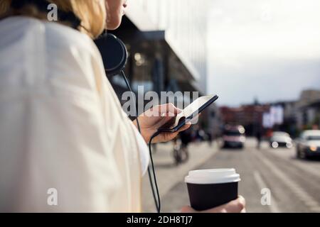 Sezione centrale della donna che usa il telefono mentre tiene la tazza di caffè dentro città Foto Stock