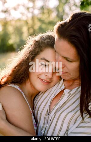 Madre sorridente che parla con la figlia mentre si abbraccia in cortile Foto Stock