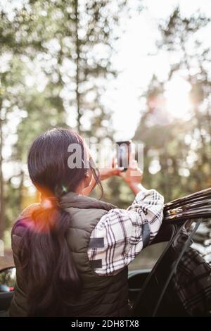 Vista posteriore di una donna che fotografa con lo smartphone in auto durante le vacanze Foto Stock