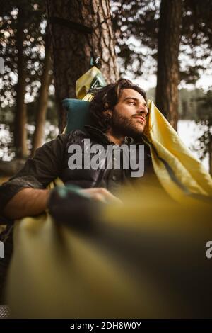 Contemplando l'uomo che guarda via mentre si sdraia sopra amaca dentro foresta Foto Stock