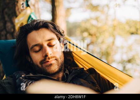 Giovane uomo con libro sdraiato su amaca in foresta Foto Stock