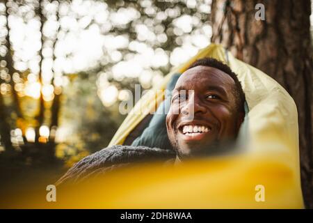 Uomo sorridente che guarda via mentre si sdraiava sopra l'amaca nella foresta Foto Stock