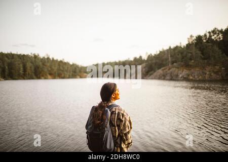 Vista posteriore di una donna sorridente in piedi contro il lago nella foresta Foto Stock