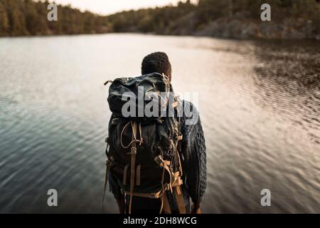 Vista posteriore dell'uomo con zaino contro il lago nella foresta Foto Stock