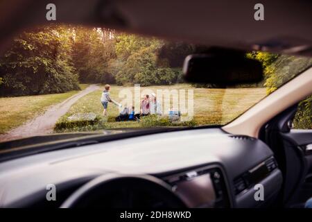 Famiglia sull'erba al parcheggio visto dal parabrezza dell'auto Foto Stock