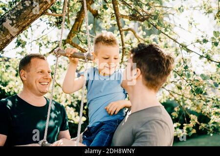 I padri omosessuali che guardano sorridere il figlio che gioca in cortile Foto Stock