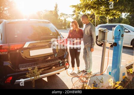 Coppia matura carica auto elettrica alla stazione in giornata di sole Foto Stock