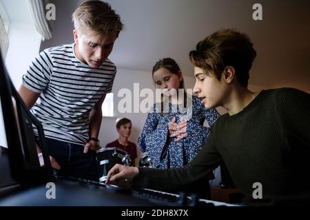 Giovane amico che spiega i fratelli mentre suona la tastiera del pianoforte a casa Foto Stock