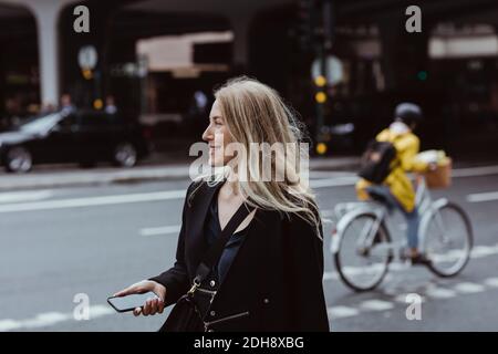 Donna d'affari sorridente con smartphone che guarda lontano in città Foto Stock