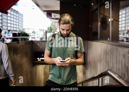 Uomo che usa il telefono cellulare mentre si cammina su passi a. stazione della metropolitana in città Foto Stock