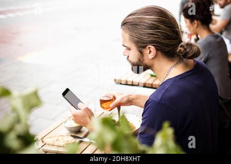 Uomo che usa il telefono cellulare mentre beve al bar sul marciapiede Foto Stock