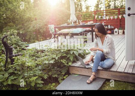 Vista ad alto angolo di una donna che utilizza il computer portatile mentre è seduto pavimento nel patio nel cortile posteriore Foto Stock