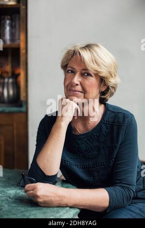 Ritratto di donna d'affari matura e sicura con la mano sulla catena seduta al tavolo del ristorante Foto Stock