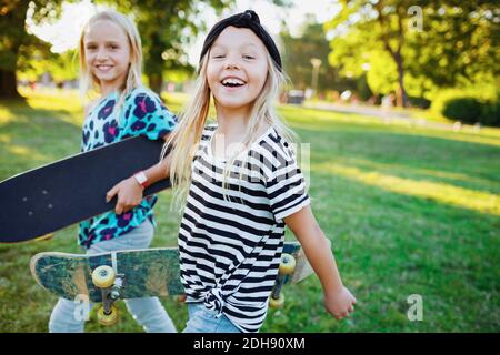 Ritratto di amici felici che trasportano skateboards mentre camminano sulla erbosa campo Foto Stock