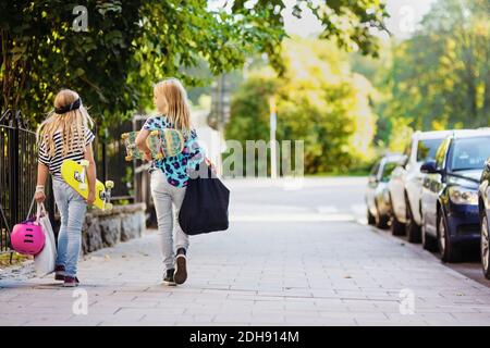 Vista posteriore delle ragazze con skateboard a piedi su strada acciottolata Foto Stock