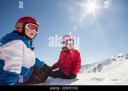Sorpresi fratelli seduti su una montagna innevata contro il cielo limpido Foto Stock