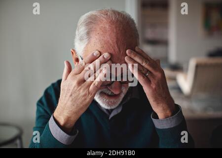 Uomo anziano preoccupato con la testa nelle mani a casa Foto Stock