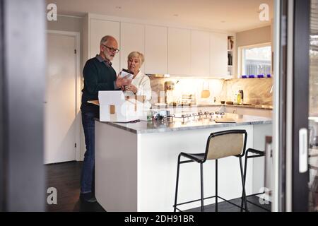 Lunghezza intera dell'uomo anziano dal socio che disimballa il pacchetto sopra isola cucina Foto Stock