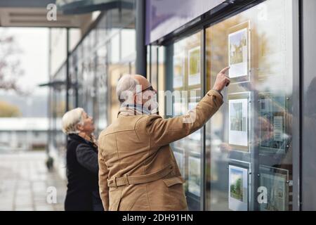 Uomo anziano che punta nella finestra di vetro dal socio femminile in città durante l'inverno Foto Stock