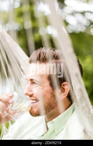 Sorridente uomo che beve mentre riposa in amaca Foto Stock