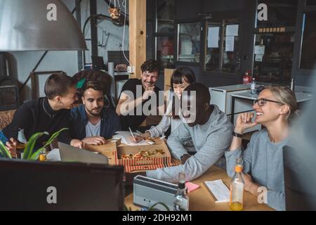 Sorridendo i colleghi che mangiano la pizza mentre lavorano sul posto di lavoro Foto Stock
