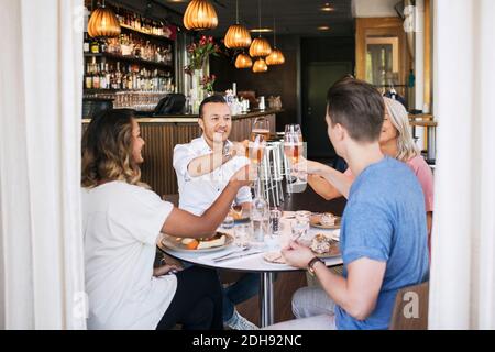 Felici gli amici che alzano il pane tostato mentre si siedono nel ristorante Foto Stock