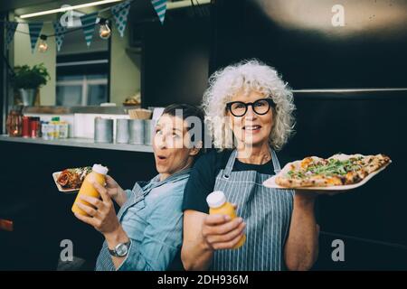 Ritratto del proprietario anziano con assistente che tiene il cibo di strada dentro città Foto Stock