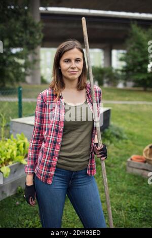 Ritratto di donna mid adulta che tiene rastrello nel giardino della comunità Foto Stock