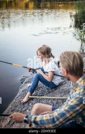 Figlia sorridente che si gode la pesca con il padre al lago Foto Stock