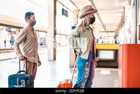 Giovane coppia in attesa in linea che pratica la distanza sociale in treno Stazione - nuovo concetto di viaggio normale con persone con viso maschera sulla coda all'interno della scrivania Foto Stock