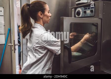 Vista laterale del putting piatto femminile chef in forno a. cucina commerciale Foto Stock