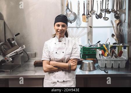 Ritratto di sorridente chef femminile con le braccia incrociate in commerciale cucina Foto Stock