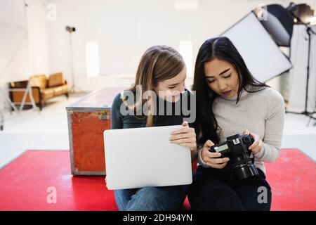 Blogger femminili che guardano le fotografie sulla macchina fotografica digitale in ufficio Foto Stock