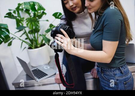 Blogger femminili che guardano le fotografie sulla fotocamera digitale in ufficio creativo Foto Stock