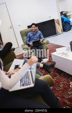 Un giovane sorridente che discute con i colleghi in ufficio creativo Foto Stock