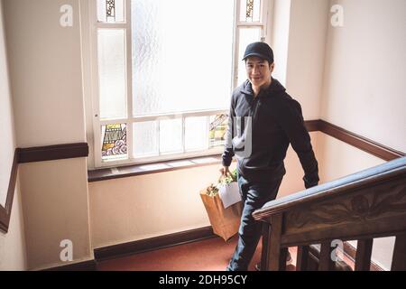 Ritratto ad alto angolo di un uomo sorridente con pacchetto contro finestra Foto Stock