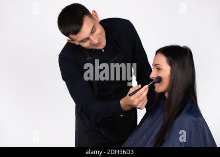 Cool maschile make-up artista facendo trucco a giovane donna d'affari. Stereotipi di bellezza, moda e genere sul bianco. Foto Stock