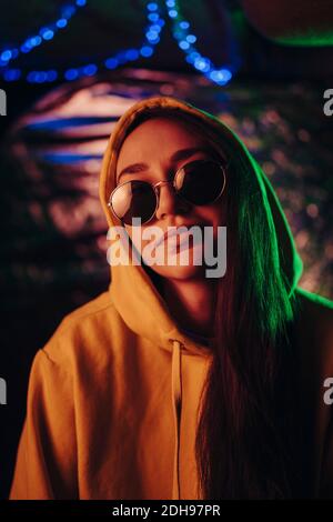 Ritratto di giovane donna sorridente che indossa occhiali da sole e cappuccio a. ristorante illuminato Foto Stock