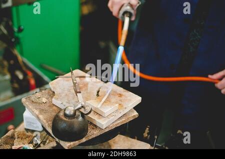 La sezione centrale dell'artigiano senior che utilizza la torcia a soffiaggio per la lavorazione dei metalli nei gioielli officina Foto Stock