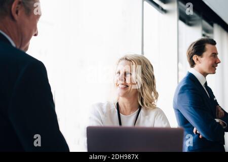 Felice imprenditore donna che parla con la collega mentre la collega sta in piedi dentro contesto sul luogo di lavoro Foto Stock