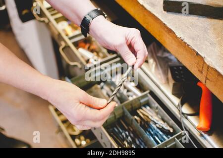 Immagine ritagliata di un'anziana persona che tiene la punta di perforazione in gioielli officina Foto Stock