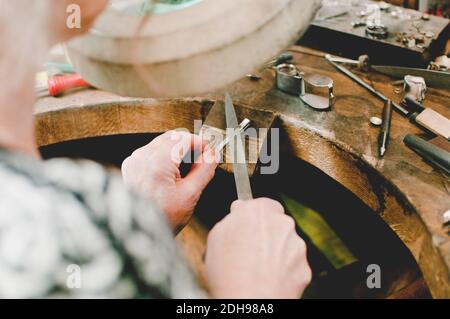 Vista ad alto angolo della gioielliera femminile senior che lavora sul banco di lavoro in officina Foto Stock